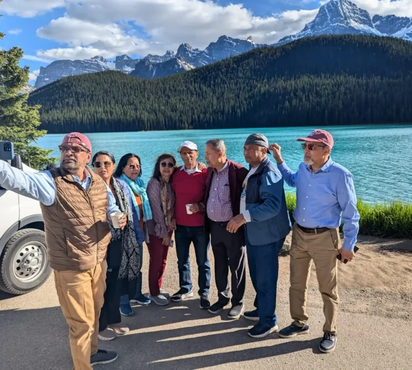 Group of travellers taking a selfie beside a shuttle van with turquoise lake and Canadian Rockies mountain views