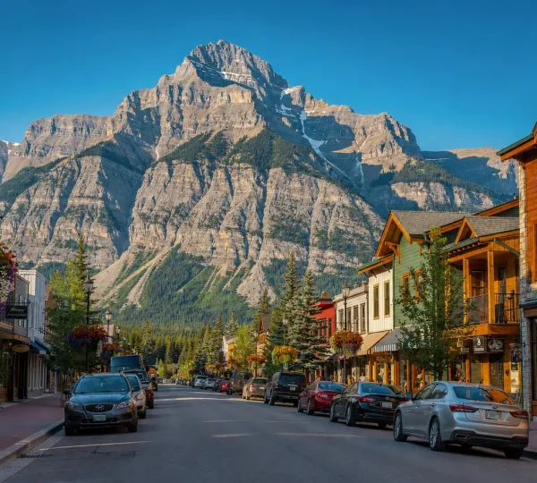 Banff Town street view with mountain backdrop, wooden shops, parked cars, and Canadian Rockies scenery