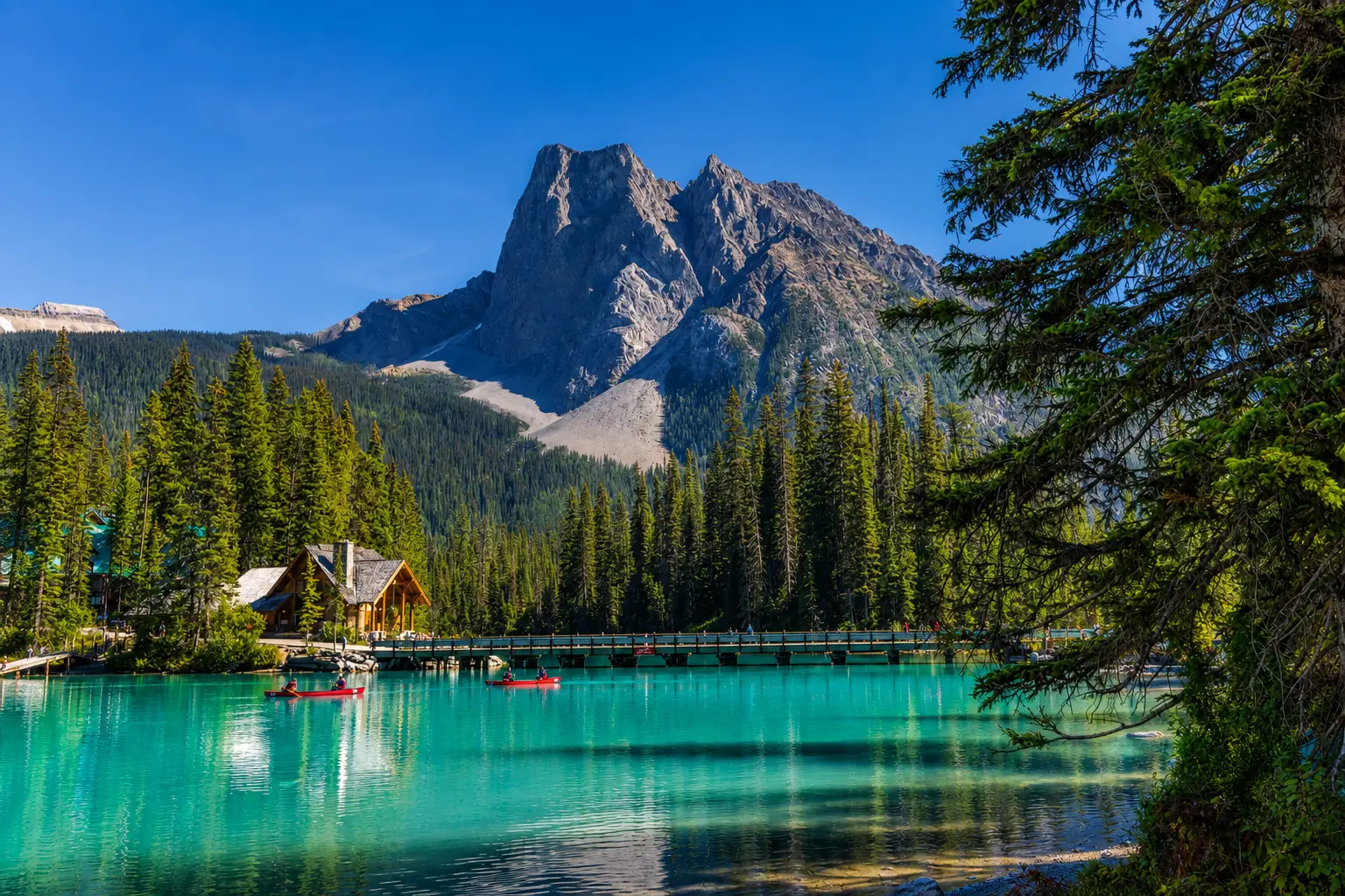 Emerald Lake scenic view with turquoise water, pine forest, mountain lodge, bridge, and Canadian Rockies landscape